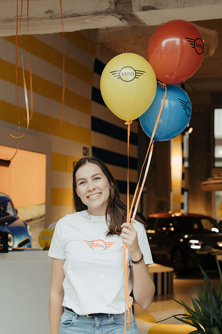 Smiling hostess holding colorful balloons with the MINI logo.