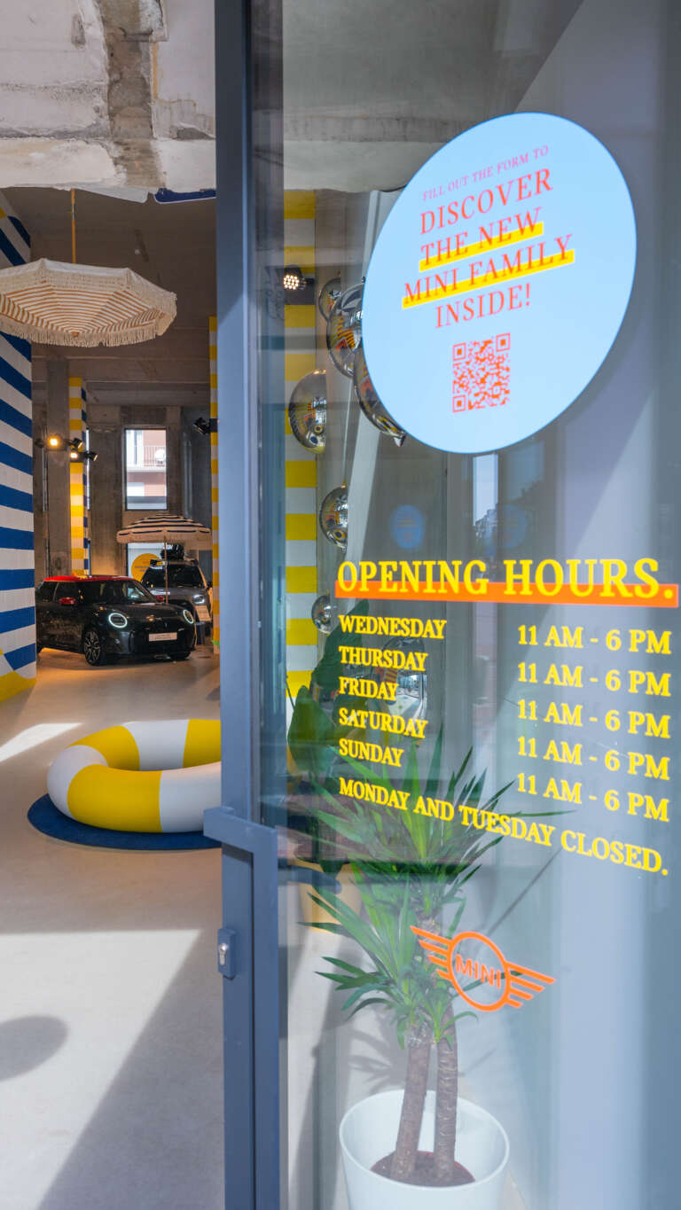 View through a glass door displaying the opening hours of the MINI pop-up space.