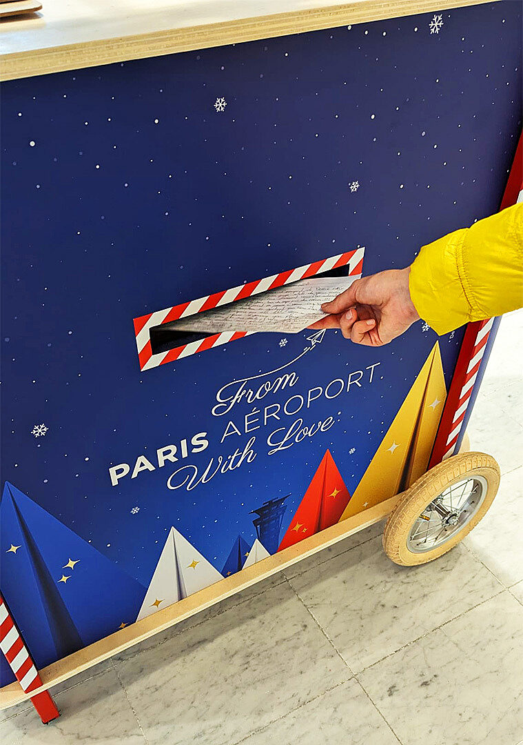 A person inserting a letter into a “From Paris Aéroport With Love” decorated mailbox.
