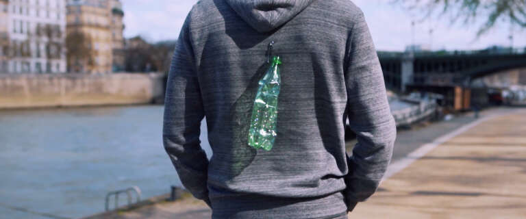 Une bouteille plastique accrochée au dos d’un passant pour dénoncer l’impact des déchets jetés dans la rue.