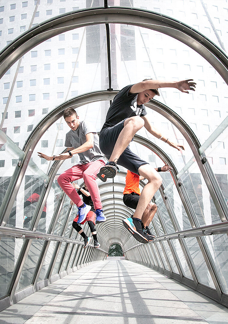 Jeunes en pleine session de parkour dans une passerelle vitrée emblématique de La Défense.