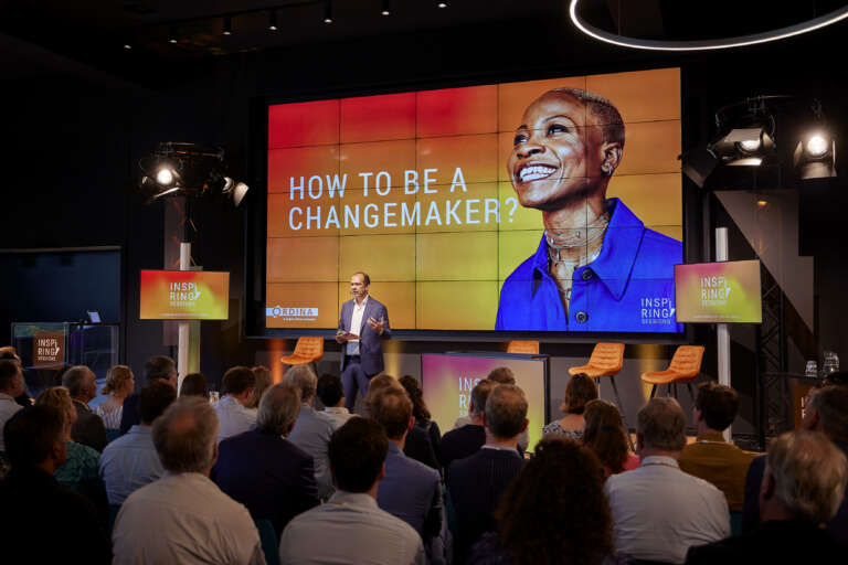 Conférence "How to be a Changemaker?" avec un intervenant sur scène et une grande photo projetée d'une femme souriante.