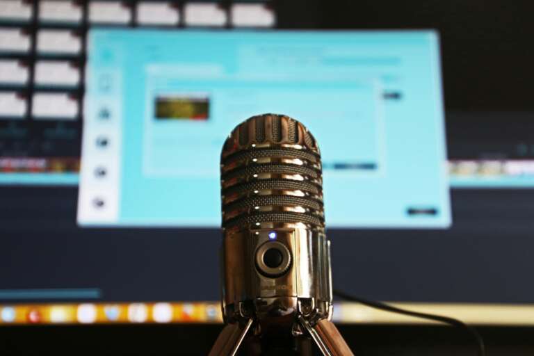 Microphone de podcast au premier plan avec un écran d’ordinateur flou à l’arrière-plan.