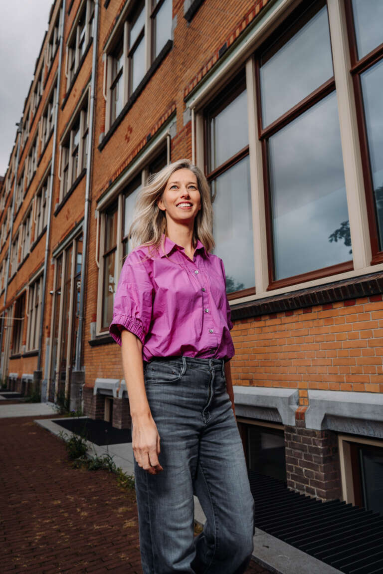 Une femme marche confiante dans une rue bordée d’immeubles en briques.