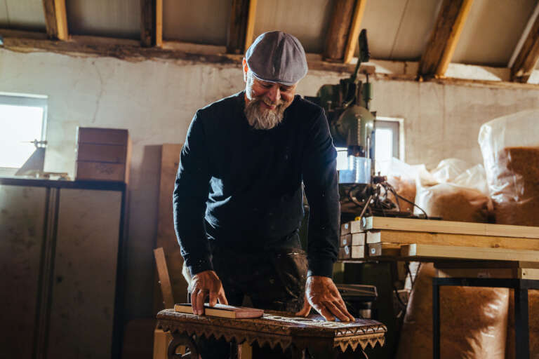 Un artisan en train de travailler minutieusement sur un meuble en bois dans son atelier.