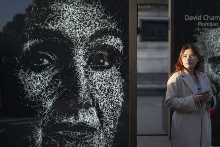 Woman walking past a striking artistic billboard showing a fractured face