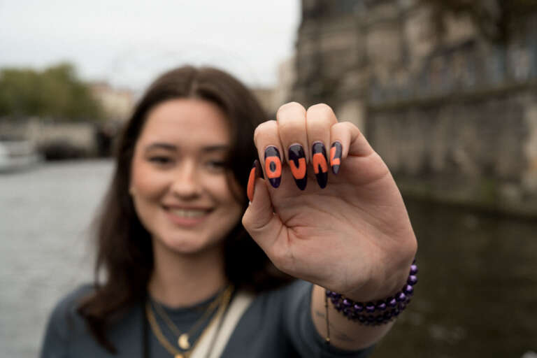 Smiling young team member proudly showing off a manicure with the letters OVAL, symbolizing agency pride and belonging